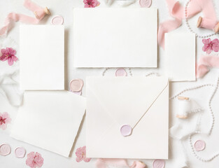 Cards and envelope near pink decorations, seals and ribbons on white table top view, wedding mockup