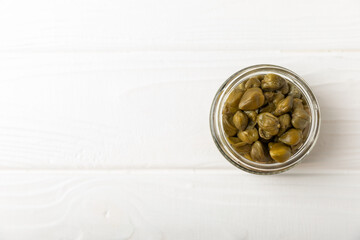 Capers in a bowl on a wooden kitchen table. Capers with sea salt and rosemary. Pickled capers.Mediterranean cuisine ingredient. Organic spices and seasonings. Copy space.