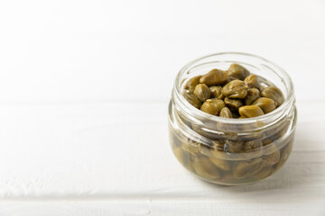 Capers in a bowl on a wooden kitchen table. Capers with sea salt and rosemary. Pickled capers.Mediterranean cuisine ingredient. Organic spices and seasonings. Copy space.