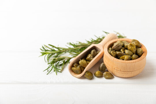 Capers in a bowl on a wooden kitchen table. Capers with sea salt and rosemary. Pickled capers.Mediterranean cuisine ingredient. Organic spices and seasonings. Copy space.