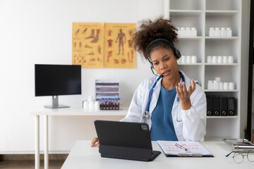 Cute smart African American female doctor wearing a headset giving online healthcare advice via...