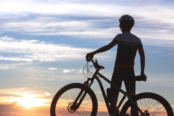 Silhouette of a cyclist next to his bike, standing still while admiring the sky and sunset in the...