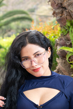 Retrato de una mujer blanca, latina, hermosa de cabello negro con chaqueta roja y una blusa azul, en frente de palmeras