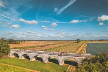 A breathtaking aerial perspective captures a majestic bridge as it spans over a vast field, connecting two distant ends in a harmonious blend of engineering and nature - obrazy, fototapety, plakaty