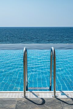 clean swimming pool Fun blue water With metal stairs located on the terrace outside the hotel against the sea and blue sky.