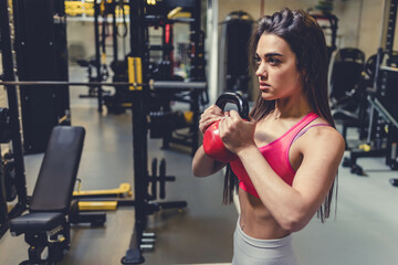 Fototapeta premium Pretty young woman exercising in gym. Young beautiful woman exercising with kettlebell in the gym.