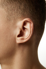 Close-up of male ear with detailed view of auricle and earlobe against white studio background. Concept of beauty procedures, male health, body care, spa treatment, hygiene.