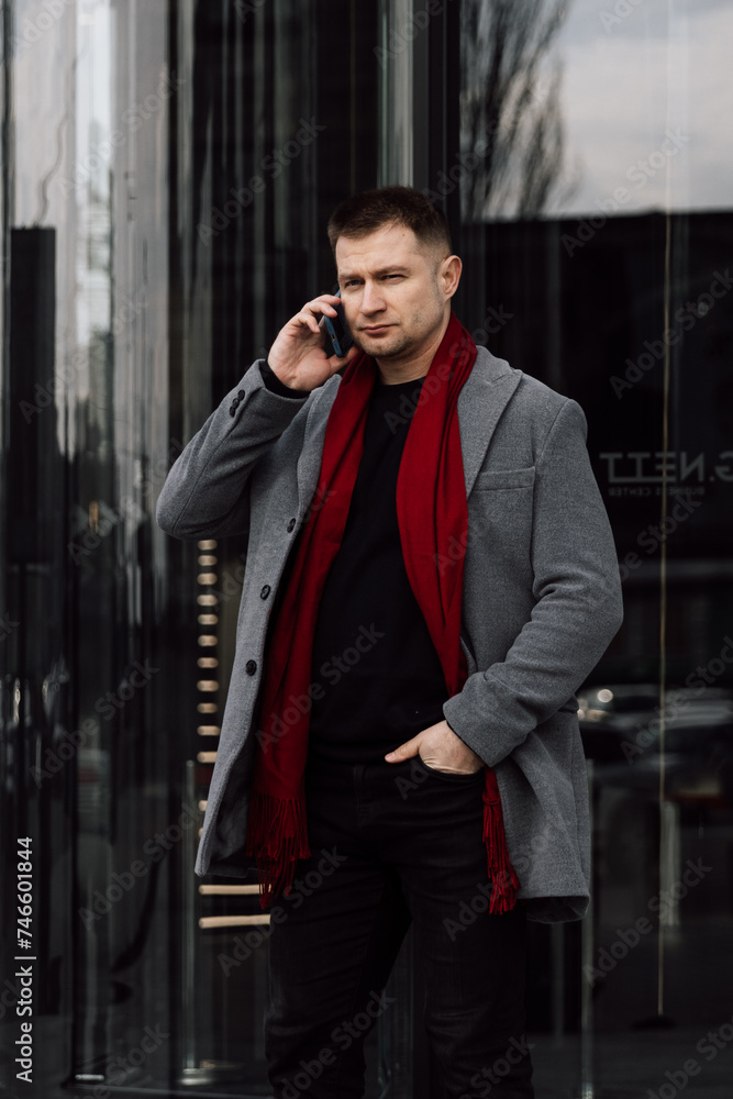 Wall mural a handsome man in a gray coat is walking on the street. businessman talking on the phone