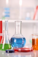 Laboratory analysis. Glass flasks and Petri dish with liquids on white table against blurred background