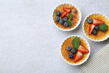 Delicious creme brulee with berries and mint in bowl on grey textured table, top view. Space for text