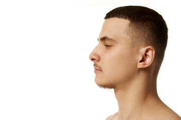 Side view headshot of young brunette shirtless man posing against white studio background....