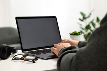 E-learning. Young man using laptop at white table indoors, closeup