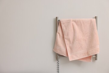 Heated rail with pink towel on white wall, space for text