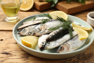 Fresh raw sprats, lemon and dill on wooden table, closeup