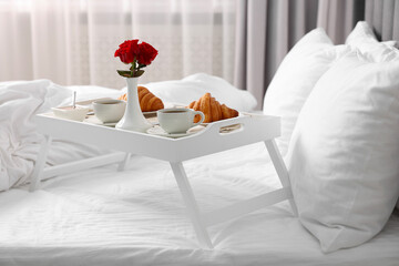 Tray with tasty breakfast and flowers on bed at home