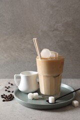 Refreshing iced coffee with milk in glass, sugar and spoon on gray table