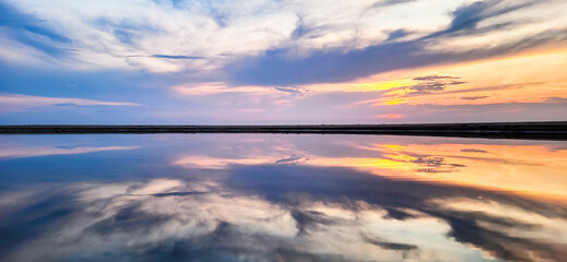 Farbenfroher Sonnenuntergang am Meer mit Spiegelung im Wasser und Wolken am Himmel in blau bis...