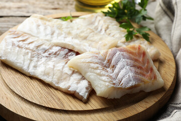 Fresh raw cod fillets and parsley on wooden table, closeup