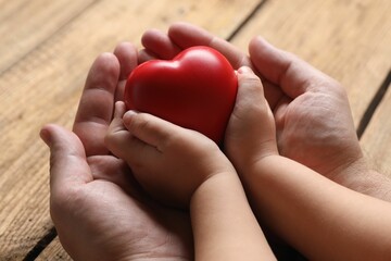 Father and his child holding red decorative heart at wooden table, closeup