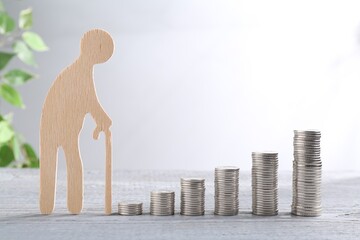 Pension savings. Figure of senior man and stacked coins on grey wooden table - obrazy, fototapety, plakaty