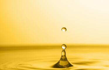 Splash of golden oily liquid with drop on yellow background, closeup. Space for text