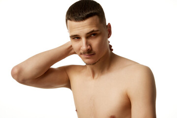 Fototapeta premium Naked handsome young man put his hand on neck and looking at camera against clear white studio background. Concept of beauty procedures, male health, body care, spa treatment, hygiene.