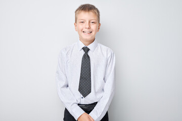 Portrait of a smiling young boy in a white shirt and tie against a light grey background.