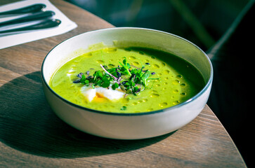 GREEN FRESH PEA ASPARAGUS CREAM SOUP SERVED ON WOODEN TABLE IN RESTAURANT, HEALTHY FOOD BACKGROUND, CLOSE VIEW