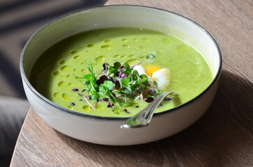GREEN FRESH PEA ASPARAGUS CREAM SOUP SERVED ON WOODEN TABLE IN RESTAURANT, HEALTHY FOOD BACKGROUND, CLOSE VIEW