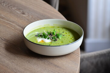 GREEN FRESH PEA ASPARAGUS CREAM SOUP SERVED ON WOODEN TABLE IN RESTAURANT, HEALTHY FOOD BACKGROUND, CLOSE VIEW
