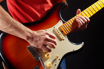 Rock guitarist in red plays the sunburst electric guitar on dark stage.