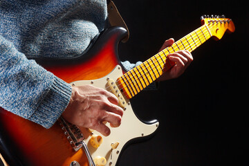 Rock guitarist in blue sweater plays the sunburst electric guitar on dark stage.