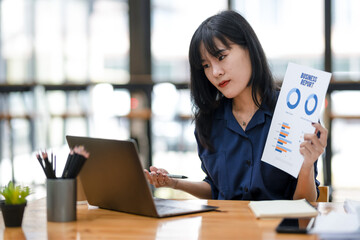 An Asian businesswoman gestures while explaining a concept during a video conference on her laptop...