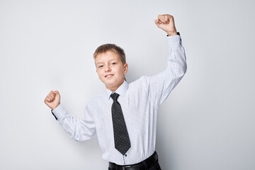 Cheerful young boy in shirt and tie celebrating success with raised fists against white background