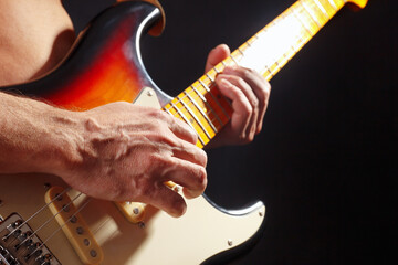 Musician playing the sunburst guitar on dark stage.
