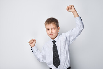 Cheerful young boy in shirt and tie celebrating success with raised fists against a white background