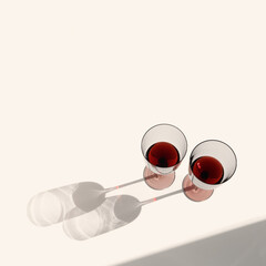 Still life with colored glass glasses of dry red wine with sunlight shadows, summer flat lay. Minimal style Two wine glasses, alcohol drink on beige background, copy space, trend photo