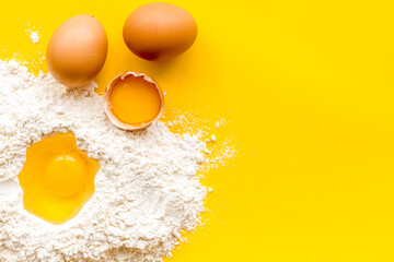 Making dough concept. Pile of flour and eggs on yellow background top view copy space