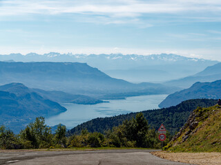 View from Grand Colombier peak towards Bourget lake and alps, asphalt road with speed limit sign (50 km/h) and warning about cow pasture area ("Alpage"), France