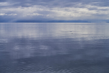 Minimalist view of an approaching rainstorm over a calm blue ocean with distant clouds and mountains