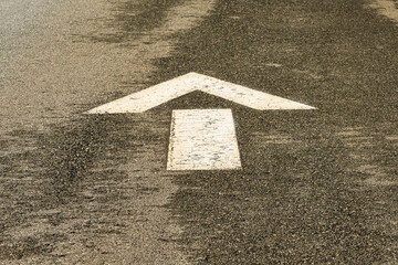 A white arrow painted on pavement indicating that the car is to go in a straight direction
