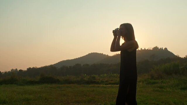 A silhouette of a young woman takes a photo in nature