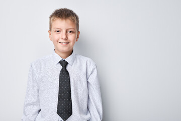 Smiling young boy in shirt and tie standing against a plain background with copy space.