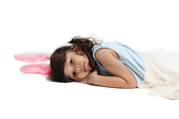 Obraz na płótnie Canvas Cute little girl wearing pink bunny ears lying down on floor. Joyful kid celebrating Easter day on white background. Happy child on Easter holiday celebration.
