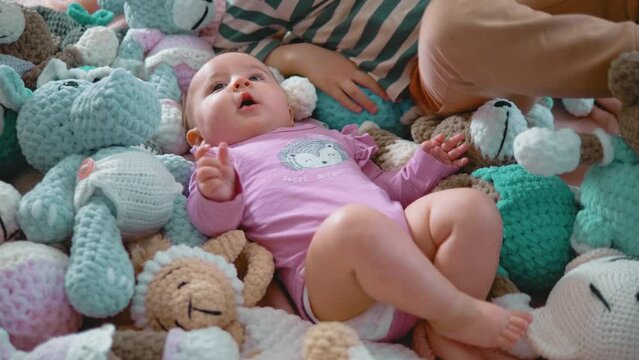 A little 3-year-old boy is playing with his newborn sister lying down among stuffed toys