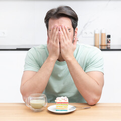 A young man sits at a table in the kitchen and suffers from the temptation to eat a delicious cake,...