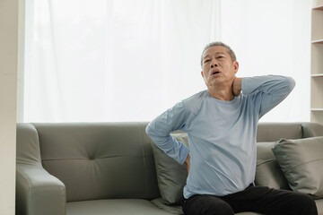 Asian elderly man has back pain and sickness in bed at home, unhappy elderly man touching his back seriously and trying, elderly care concept