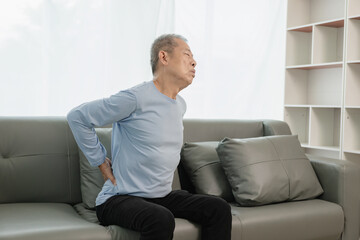 Fototapeta premium Asian elderly man has back pain and sickness in bed at home, unhappy elderly man touching his back seriously and trying, elderly care concept