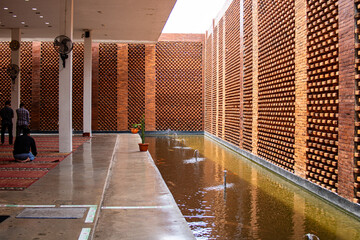 Modern interior of semi outdoor mosque (masjid) with unique exposed red brick facade and pond on...
