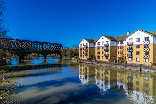 A view along the north shore of the River Nene towards the historic railway bridge in Peterborough, UK on a bright sunny day
